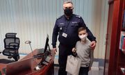 umundurowany policjant stoi z chłopcem w pokoju w Komendzie Powiatowej, chłopiec trzyma w ręku torebkę ozdobną z prezentem