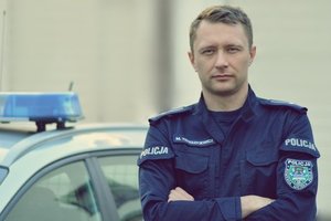 Mł. asp. Marcel Tereszkiewicz w tle radiowóz