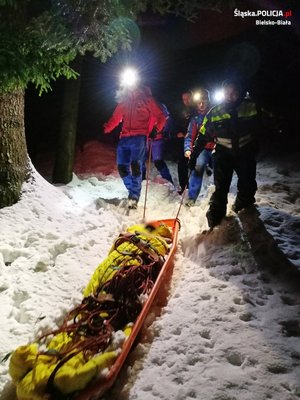 Ratownicy po śniegu w lesie prowadzą nosze z poszkodowanym. Zdjęci wykonane w nocy zimą