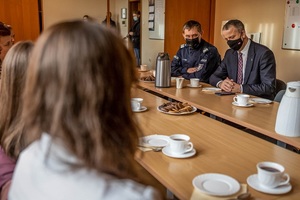 dwie dziewczynki siedzą przy stole, a naprzeciwko nich siedzi mężczyzna i umundurowany policjant