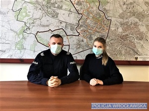 policjant i policjantka siedzą przy stole, w tle na ścianie mapa