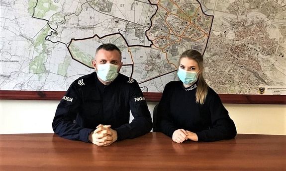 policjant i policjantka siedzą przy stole, w tle na ścianie mapa