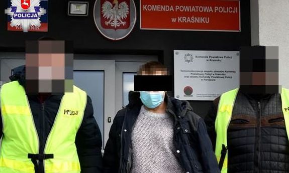 dwóch funkcjonariuszy prowadzi zatrzymanego mężczyznę, w tle budynek komendy powiatowej policji