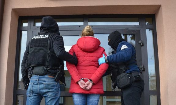 dwaj policjanci i zatrzymana kobieta w kajdankach przed wejściem do komisariatu policji