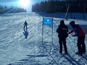 widok na stok narciarski na którym po prawej stronie stoi funkcjonariusz policji wraz z ratownikiem GOPR