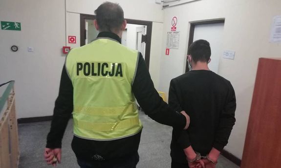policjant w odblaskowej żółtej kamizelce z czarnym napisem na plecach policja prowadzi zatrzymanego mężczyznę