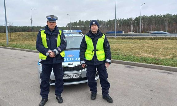 dwaj policjanci, którzy eskortowali 9-ciomiesięczne dziecko do szpitala w Szczecinie, od lewej sierż. szt. Mirosław Pawelec i post. Grzegorz Idziaszek na tle radiowozu oznakowanego Kia Ceed