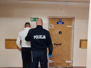 umundurowany policjant z zatrzymanym przed policyjną celą