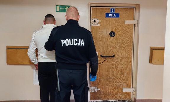 umundurowany policjant z zatrzymanym przed policyjną celą