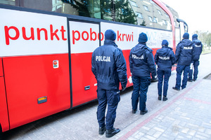 umundurowani policjanci stoją w kolejce przy mobilnym punkcie poboru krwi  - widok z tyłu