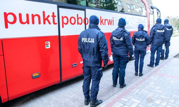 umundurowani policjanci stoją w kolejce przy mobilnym punkcie poboru krwi  - widok z tyłu