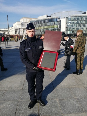 policjant trzyma pamiątkową tabliczkę w etui