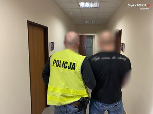 Policjant z zatrzymanym na korytarzu, stroją tyłem