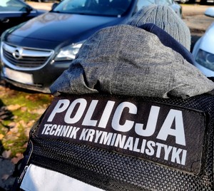 Na pierwszym planie Policjant z napisem Policja technik kryminalistyki, z tyłu widać zabezpieczony samochód