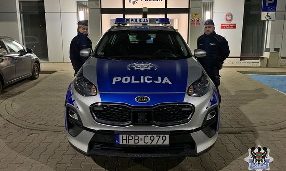 dwoje umundurowanych policjantów stojących przy radiowozie