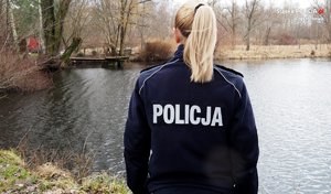 policjantka stoi tyłem do fotografującego, patrzy na taflę wody zbiornika wodnego