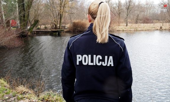 policjantka stoi tyłem do fotografującego, patrzy na taflę wody zbiornika wodnego