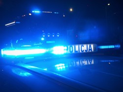 Noc. Świecące światła na dachu radiowozu i napis Policja na belce