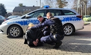 policjanci z uratowaną kobietą, w tle radiowóz policyjny