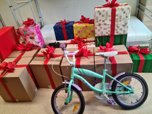 ułożone w pomieszczeniu opakowane jak prezenty zebrane produkty spożywczo-przemysłowe i rowerek dla dziecka