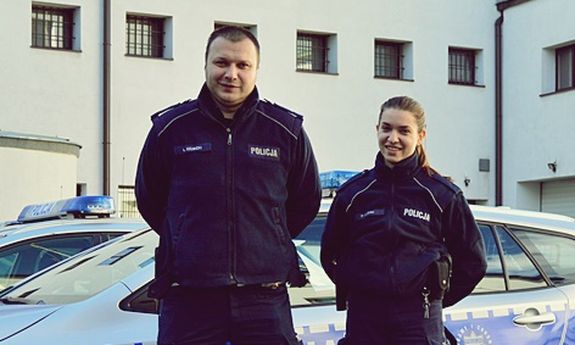 policjant i policjantka stoją przed radiowozem