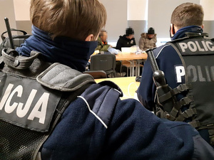 w pomieszczeniu siedzą dwaj policjanci i trzej uchodźcy