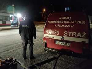 Policjant w mundurze stoi w nocy przy samochodzie grupy poszukiwawczej