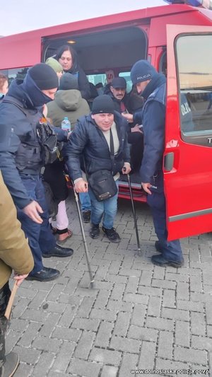 policjanci pomagają uchodźcom wysiadającym z busa
