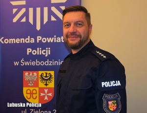 umundurowany policjant pozuje do zdjęcia na tle banera z napisem Komenda Powiatowa Policji w Świebodzinie
