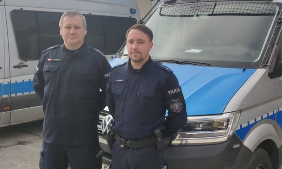 dwaj policjanci stoją przy radiowozie