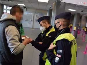 policjanci w niebieskich mundurach i odblaskowych kamizelkach udzielają informacji mężczyźnie w jasnej bluzie z kapturem i czarnej kamizelce