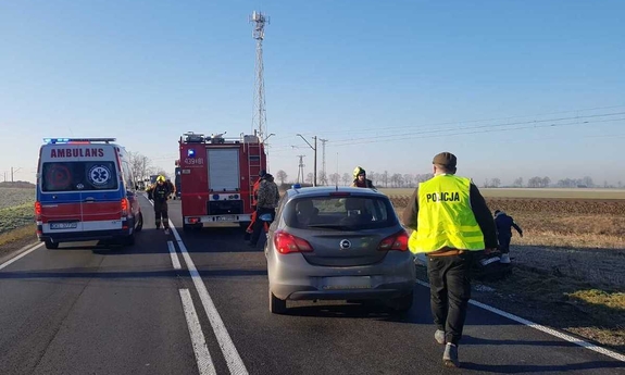 widok na pojazdy służb ratunkowych stojące na drodze i pracujących na miejscu policjantów i strażaków