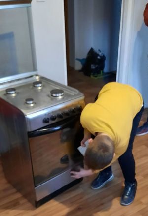 Młody chłopiec wyciera dół kuchenki gazowej ściereczką