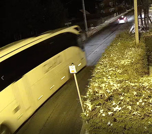 print screen z nagrania kamery  miejskiego monitoringu - biały autokar jadący drogą przed nim policyjny radiowóz