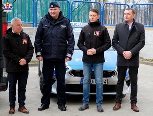 umundurowany policjant i trzej mężczyźni stoją przed radiowozem