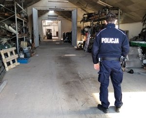 Policjant na miejscu odnalezienia utraconego pojazdu, teren warsztatu samochodowego