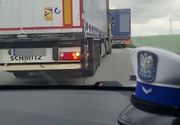 widok z wnętrza radiowozu przez szybę czołową na pojazdy ciężarowe stojące w zatorze drogowym, po prawej stronie na podszybiu widoczna czapka policjanta ruchu drogowego, przed samochodem