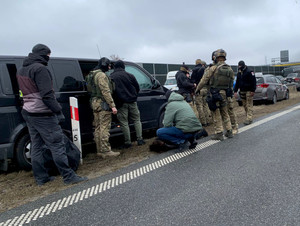 umundurowani i nieumundurowani policjanci stoją na poboczu jezdni i na jezdni przy stojących pojazdach