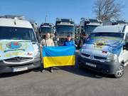 dwaj mężczyźni z flagą Ukrainy stoją pomiędzy dwoma autami, które na maskach maja rozłożone flagi IPA