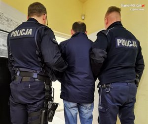 dwaj umundurowani policjanci prowadzą korytarzem zatrzymanego - stoją tyłem do fotografującego