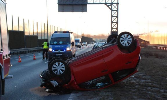 leżący na dachu samochód, policjanci pracujący na miejscu zdarzenia