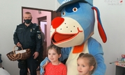 Sznupek pozuje do zdjęcia z dwiema dziewczynkami, obok stoi policjant z koszem w którym są słodycze