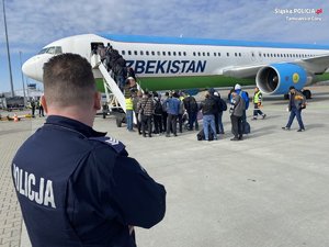 policjant w niebieskim mundurze obserwuje pasażerów wsiadających do samolotu
