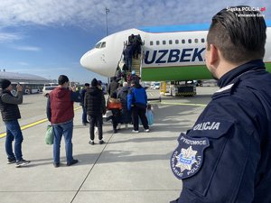 policjant w niebieskim mundurze, na lewym ramieniu naszywka z napisem Pyrzowice komisariat policji obserwuje pasażerów wsiadających do samolotu