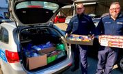 policjanci w mundurach stoją przy radiowozie trzymając w rekach pudełka z produktami, bagażnik wypełniony produktami spożywczymi i chemicznymi