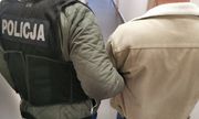 Policjant w ubraniu cywilnym w kamizelce z napisem policja trzyma zatrzymanego mężczyznę