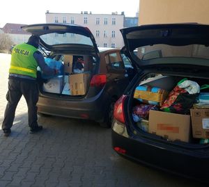 policjant wkłada paczkę do jednego z dwóch stojących aut, wypełnionych darami