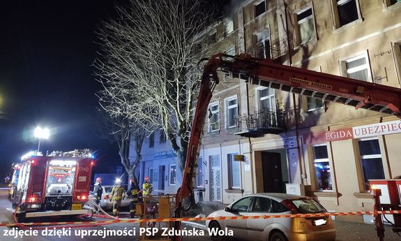 miejsce akcji gaśniczej, strażacy gaszą pożar kamienicy, na ulicy stoją wozy strażackie