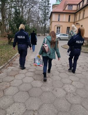 dwie umundurowane policjantki, w tym jedna niesie na ręku dziecko, między nimi idzie matka dziecka