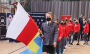 policjantka niesie flagę biało-czerwoną, za nią idzie kobiecy zespół biorący udział w turnieju